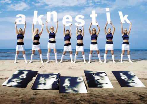Aknestik-bändin promokuva, jossa hiekkarannalla juuri ennen vesirajaa seisoo lauma samanlaisiin asuihin pukeutuneita hymyileviä naisia, joilla käsissään päidensä yllä bändin nimikirjaimet. Jokaisella naisella yksi kirjain kourissaan.