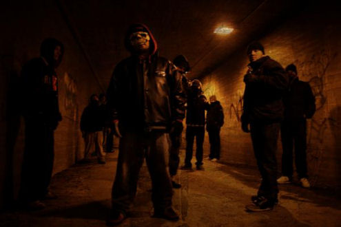 OG Ikosen &quot;possesta&quot; otettu valokuva. Kuvassa näkyy lauma miehiä seisomassa hämärässä tunnelissa, jonka seinillä palaa oransseja lamppuja. Valtaosa heistä pukeutunut mustiin tai tummiin vaatteisiin.