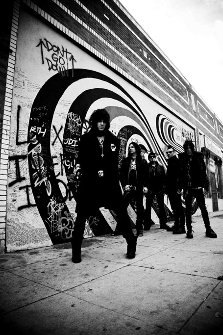 The 69 Eyesin jäsenet harmaasävyisessä ja voimakkaalla kontrastilla varustetussa bändikuvassa. Miehistö seisoo ulkoilmassa spreijatun ja sotketun seinän edustalla betonikadulla.